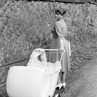 Woman stands with vintage baby carriage outdoors.