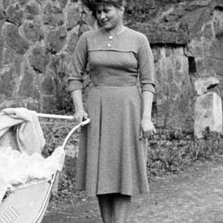 Woman walking along a path, pushing a vintage baby carriage.