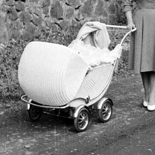Woman walking along a path, pushing a vintage baby carriage.