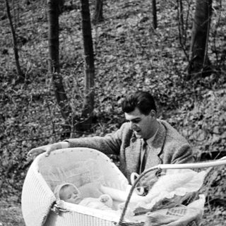 Man pushing a baby in a wicker stroller outdoors.