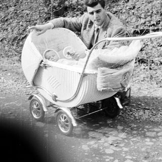 Man pushes a baby in a vintage wicker stroller.