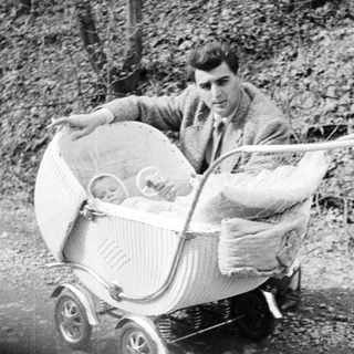 Man pushes a baby in a vintage wicker stroller.