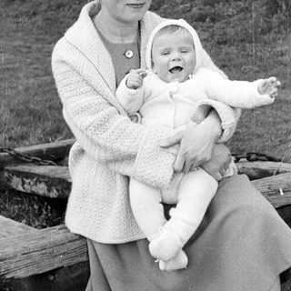 Woman holding a smiling baby outdoors in a black and white photo.