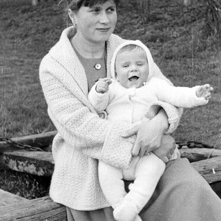 Woman holding a smiling baby outdoors in a black and white photo.