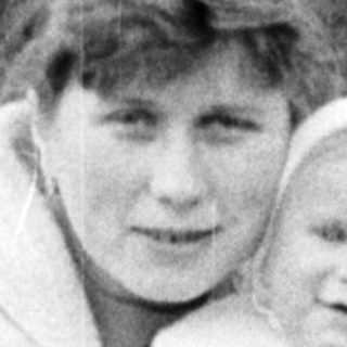 Woman holding a baby, seated on a wooden fence.
