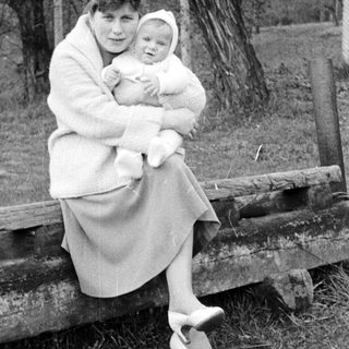 Woman holding a baby, seated on a wooden fence.