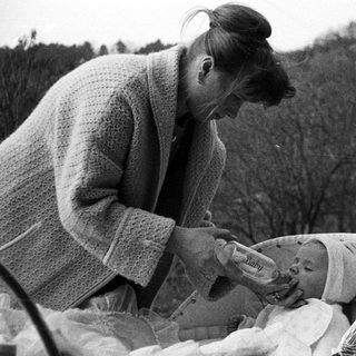 Woman feeds a baby outdoors in a basket.