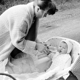 Woman tending to a baby in a vintage wicker carriage.