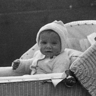 Woman and baby in a wicker carriage outdoors.