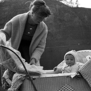 Woman and baby in a wicker carriage outdoors.