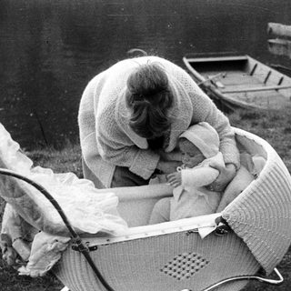 Woman tending to a baby in a vintage wicker stroller.
