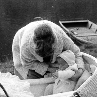 Woman tending to a baby in a vintage wicker stroller.