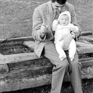 Man sits on a fence holding a baby.