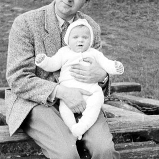 Man sits holding a baby on a wooden bench.