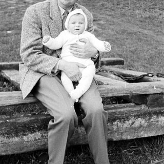 Man sits holding a baby on a wooden bench.