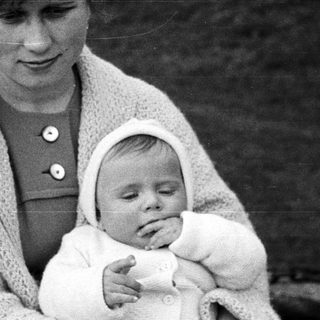 Woman holds sleeping baby outdoors in a vintage photograph.