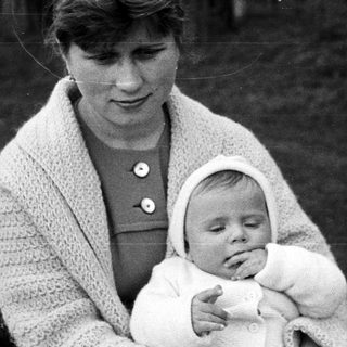 Woman holds sleeping baby outdoors in a vintage photograph.