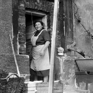 Woman in apron stands in doorway, likely in a kitchen.