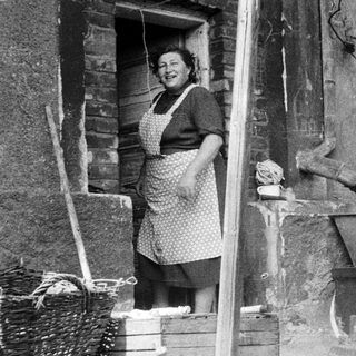 Woman in apron stands in doorway, likely in a kitchen.