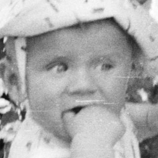 Baby in a hat is being observed by a woman.