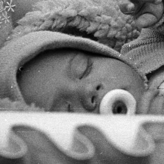 Here's a brief summary of the image: Infant sleeps peacefully in a vintage crib.