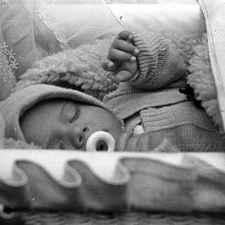 Here's a brief summary of the image: Infant sleeps peacefully in a vintage crib.