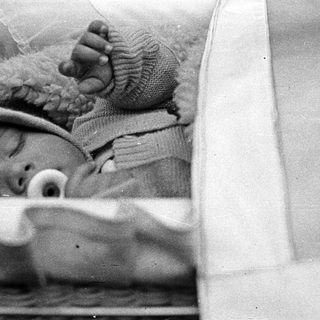 Baby sleeps peacefully in a crib, wearing a hat.