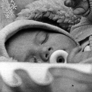 Baby sleeps peacefully in a crib, wearing a hat.
