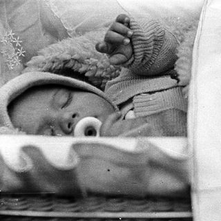 Baby sleeps peacefully in a crib, wearing a hat.