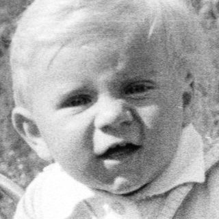Baby sits in a vintage stroller outdoors.
