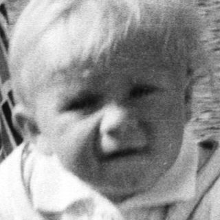 Baby in vintage stroller, captured in black and white.