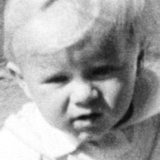 Baby sits in vintage stroller, likely outdoors.