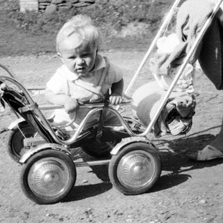 Baby sits in vintage stroller, likely outdoors.