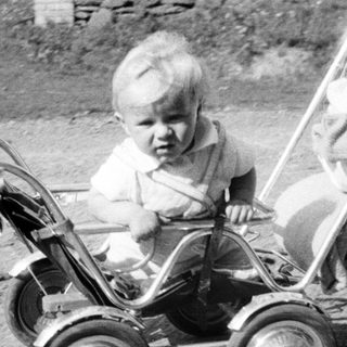 Baby sits in vintage stroller, likely outdoors.