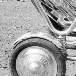 Here's a brief summary of the image: Baby standing in vintage stroller outdoors, looking away.