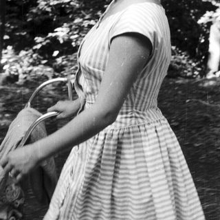 Woman in striped dress walks outdoors, carrying a basket.