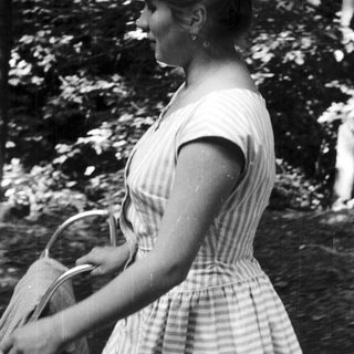 Woman in striped dress walks outdoors, carrying a basket.