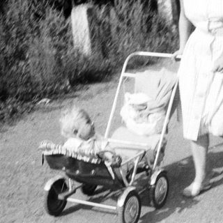 Woman pushing a baby in a vintage stroller.