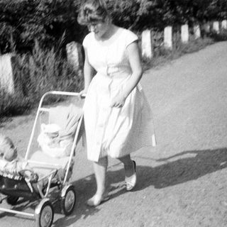 Woman pushing a baby in a vintage stroller.