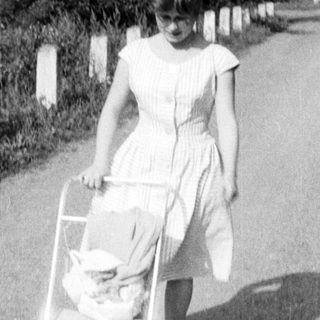Here's a brief summary of the image: Young woman walks along a road, pushing a baby carriage.