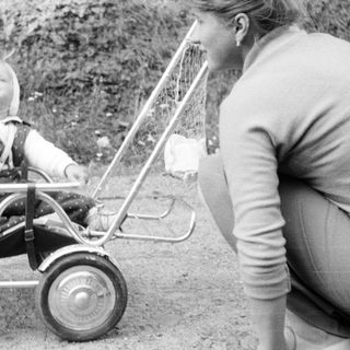 Baby in a pram with a woman nearby.