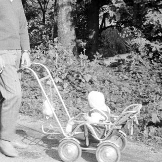 Man stands outdoors, pushing a baby carriage on a path.