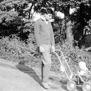 Man stands outdoors, pushing a baby carriage on a path.