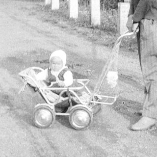Man stands beside a baby in a vintage stroller.