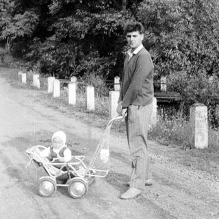 Man stands beside a baby in a vintage stroller.