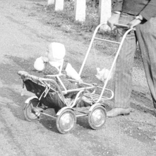 Man pushing a vintage lawnmower down a country road.