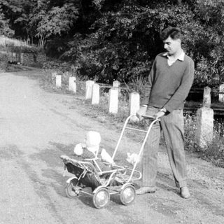 Man pushing a vintage lawnmower down a country road.
