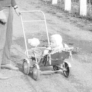 Boy standing near a baby carriage on a dirt road.