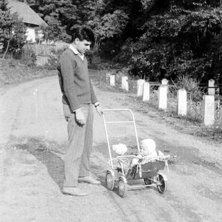Boy standing near a baby carriage on a dirt road.