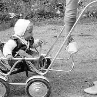 Baby in a vintage stroller, outdoors, monochrome photograph.